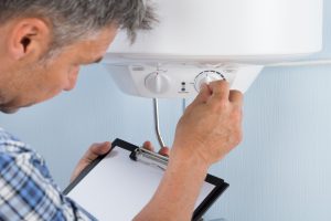 A plumber inspecting and turning the knob of a heater