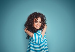 confident smiling woman hugging herself against sky blue background