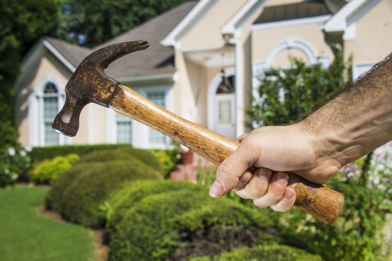 man holding hammer in front of home concept of home maintenance