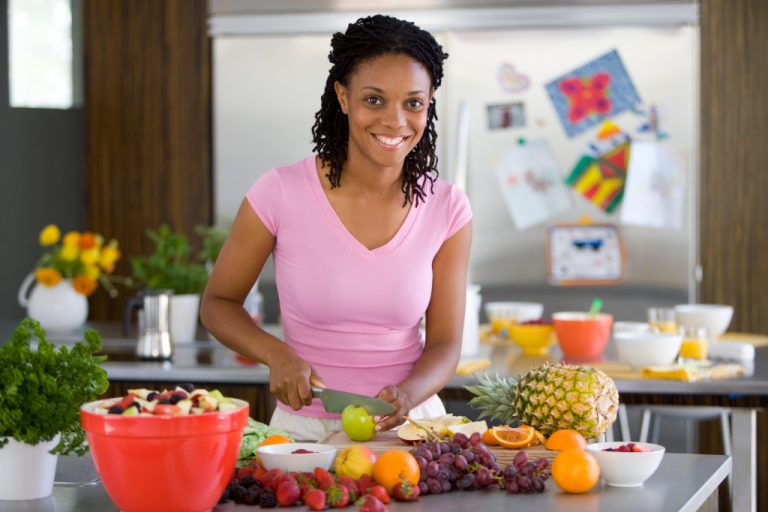 A smiling woman cutting up fruits for salad while smiling
