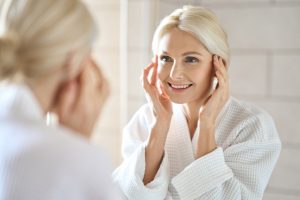 A middle-aged woman happily looking at her skin in the mirror for her beauty routine