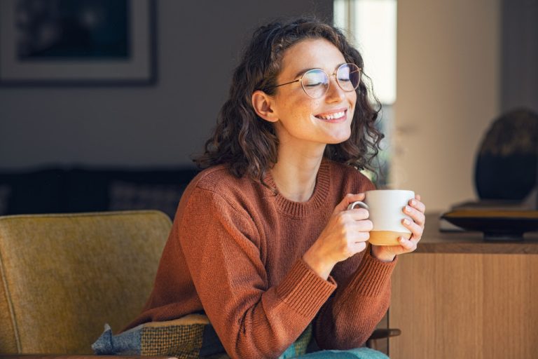 Young smiling woman feeling confidently safe at home while having a cup of coffee.