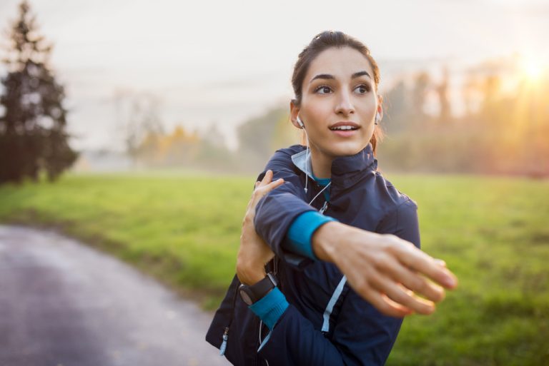 smiling woman while looking away and stretching before a run in the morning outdoors